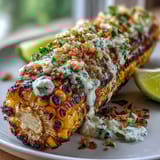 Grilled corn elote style with creamy sauce, Cotija cheese, and chili powder on a platter.