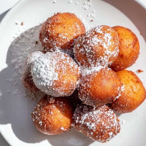 Warm, bite-sized doughnut holes fresh from the fryer, ready to be coated in cinnamon sugar.