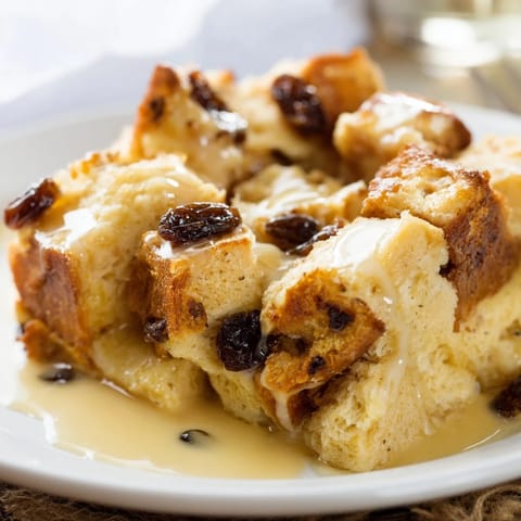 Golden-brown bread pudding, a classic American dessert, warm and drizzled with creamy sauce.