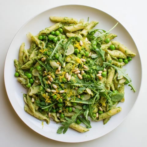 Spring Green Pesto Pasta Salad in a serving bowl, mixed with bright green peas, peppery arugula, and toasted pine nuts.