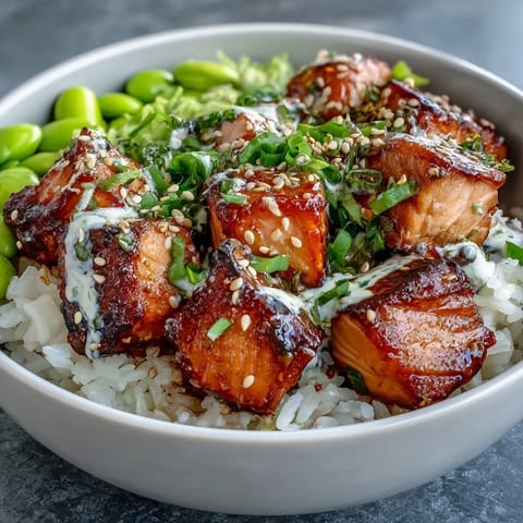 Golden-baked salmon cubes glisten atop fluffy jasmine rice in a vibrant Salmon Rice Bowl, garnished with edamame and sliced avocado.