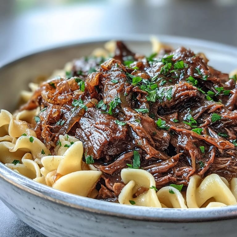 Melted Gruyère cheese blankets tender beef and onions piled over noodles in Crockpot French Onion Pot Roast Pasta serving.