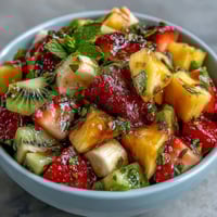 Vibrant tropical fruit salad with juicy pineapple, mango, and papaya in refreshing mint lime dressing.  