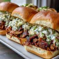 Tender BBQ pulled pork piled high on soft slider buns, topped with creamy coleslaw for a flavorful bite.  