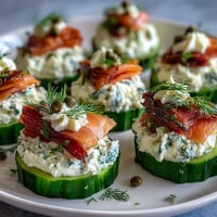 Cucumber bites topped with cream cheese and smoked salmon, garnished with dill and capers for an elegant appetizer.  
